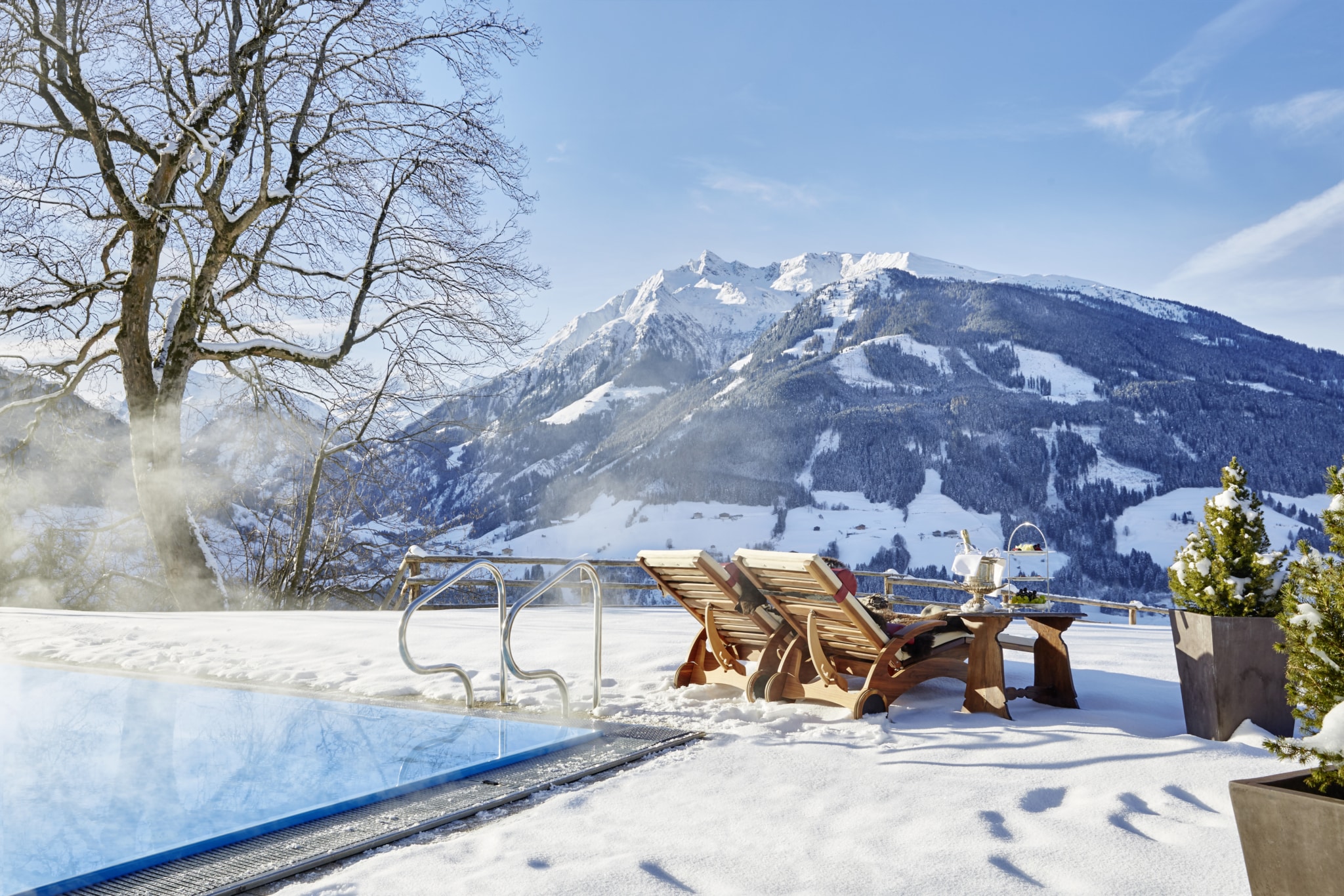 Wellness im beheizten Pool mit Aussicht auf die winterliche Bergwelt und feinen Ruheliegen