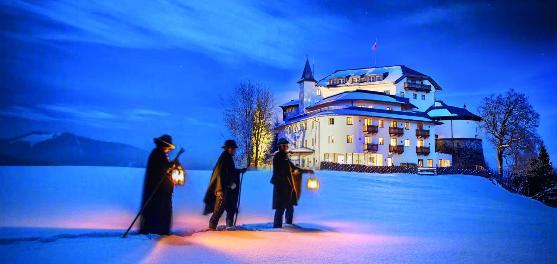 Anglöckler in traditioneller Tracht vor dem festlich beleuchteten Schloss Mittersill zur Weihnachtszeit.