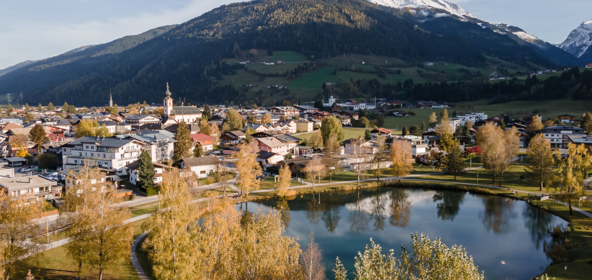 Landschaftsbild von Mittersill aus Vogelperspektive in Herbstlicher Stimmung. Mittersiller Zierteich, Stadt, Berggipfel im Hintergrund